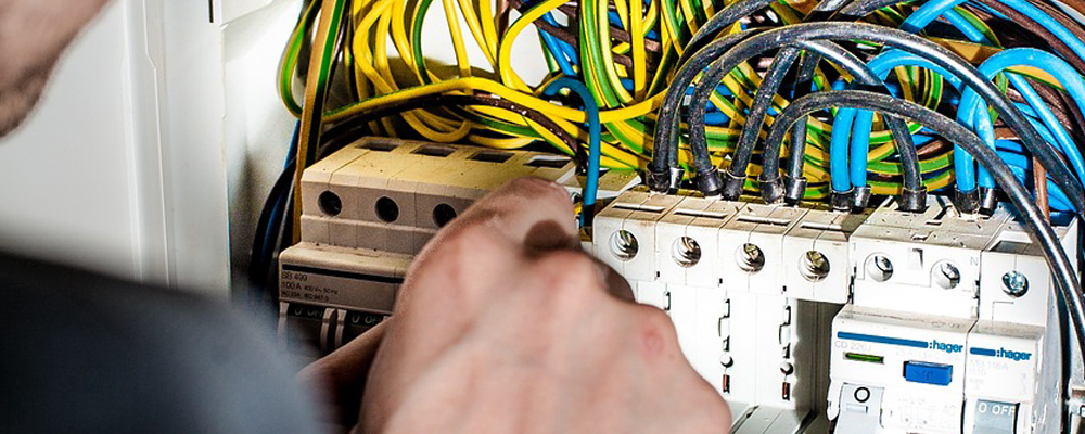 electrician repairing electrical box with connection cables and using screwdriver in corridor