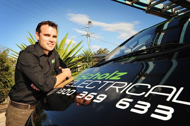 Michael Scholz, owner of Scholz Electrical is leaning on the hood of an electrician van printed with Scholz Electrical's brand logo