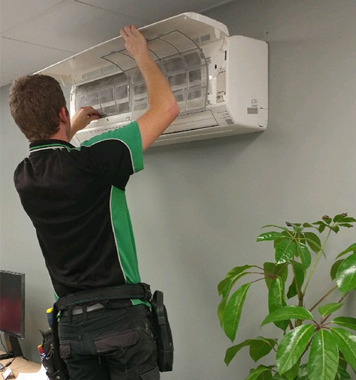 Scholz Electrical's electrician cleaning an air conditioning unit filter